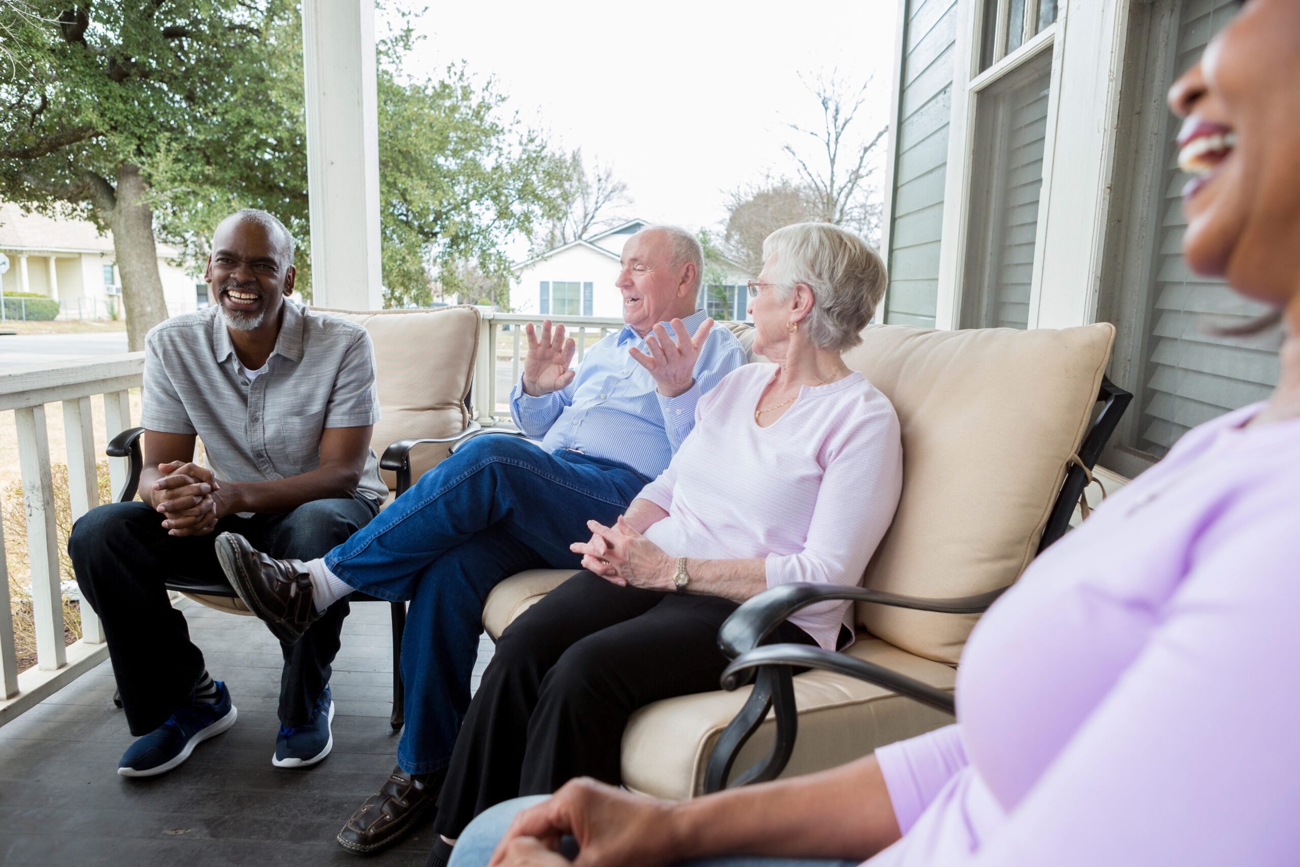 Two senior couples sitting on an outdoor cushioned couch at a manufactured home porch