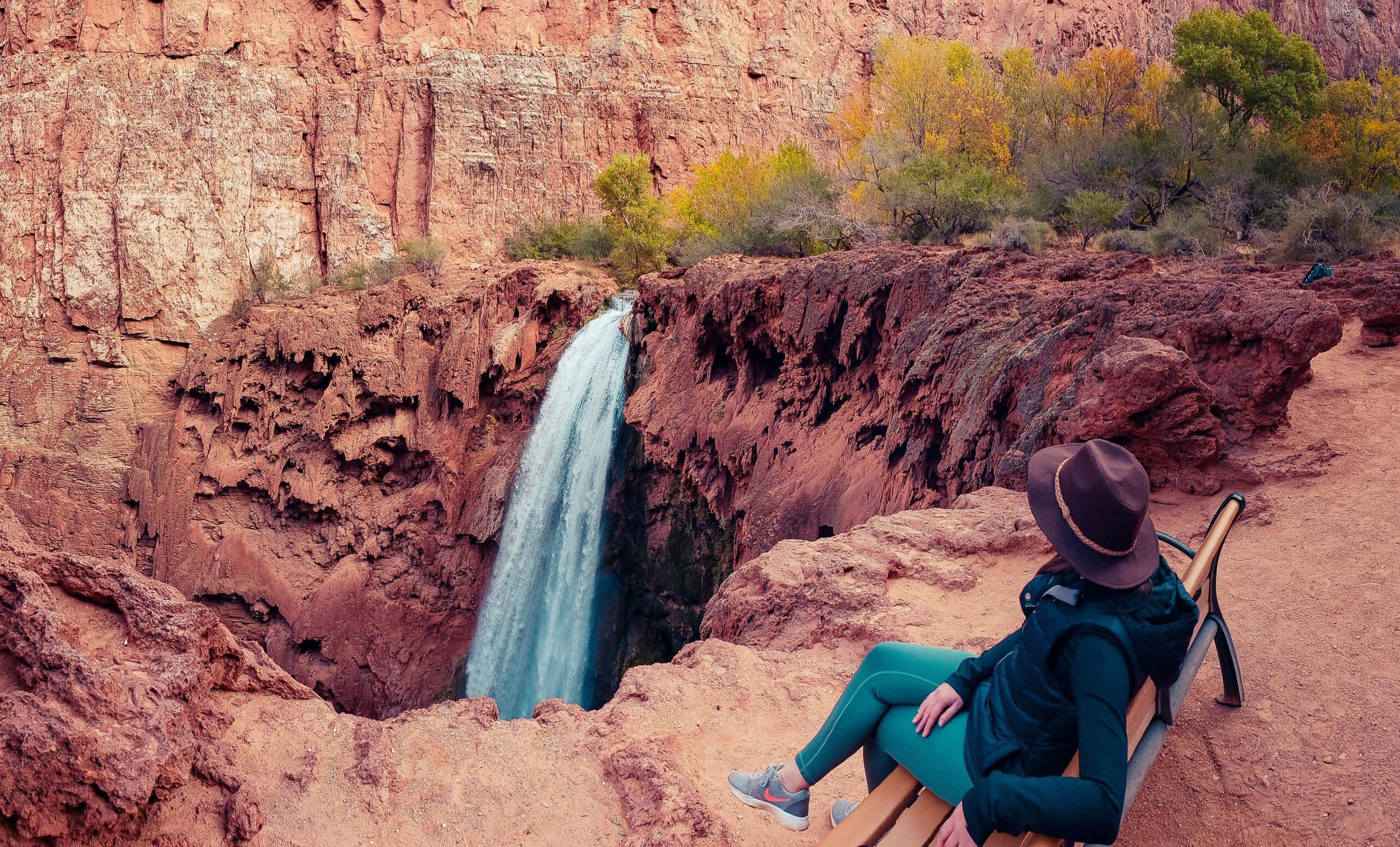 Lady sitting on a wooden bench observes a waterfall in an Arizona desert trail