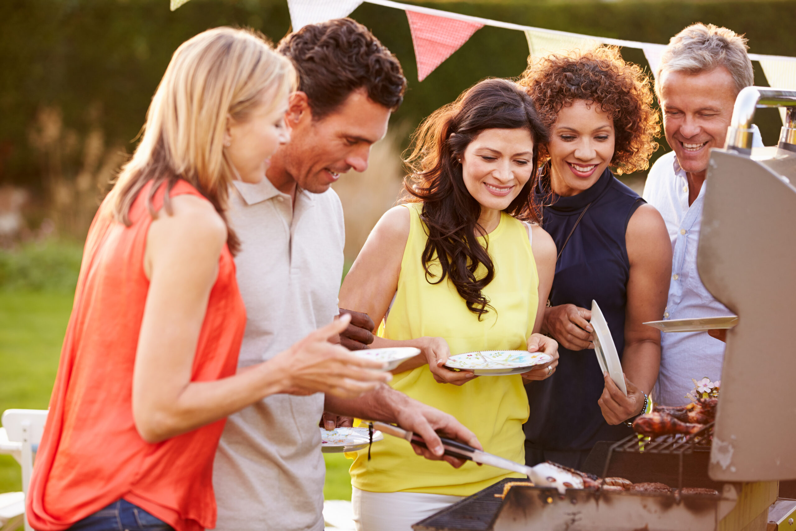 Five persons are serving themselves food from a grill at an outdoor BBQ event