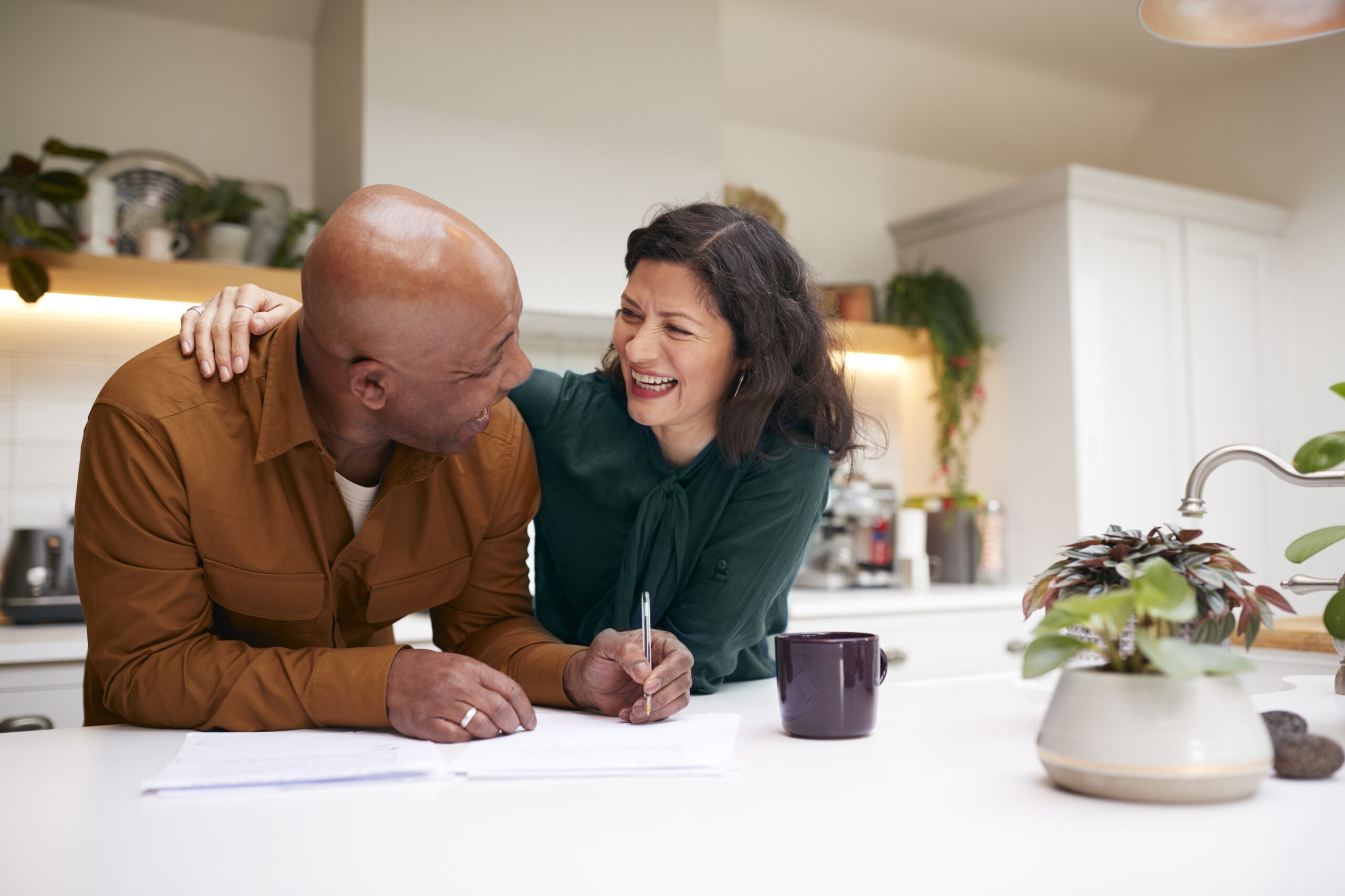 Smiling couple reviewing documents together at a kitchen counter with plants in the background in Arizona