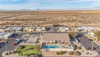 Aerial view of a mobile home community with a central pool, clubhouse, and parking, set in a desert landscape.