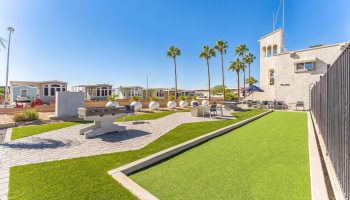 Outdoor game area with putting green, ping pong table, and palm trees under clear blue sky in Arizona